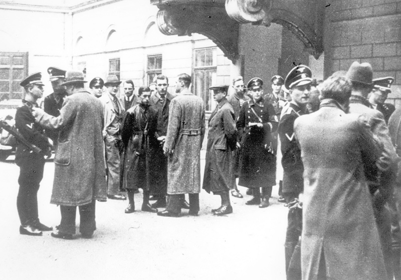 Black and white photograph of men in coats and uniformed SS guards standing in a courtyard in Vienna.